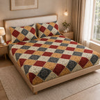 A bed dressed in a patchwork quilted bedspread and matching pillow shams, styled in a warm, modern bedroom setting with wooden furniture, bedside tables, and warm lighting.
