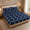 A neatly made bed in a warm, modern bedroom setting, featuring a navy blue and white geometric patterned sheet set with matching pillowcases.