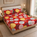 A bed dressed in a red bedding set with a bold retro pattern of concentric circles in yellow, pink, white, and dark red, styled in a modern bedroom setting.