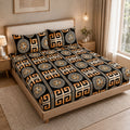 A bed dressed in a black bedding set with a bold geometric and medallion pattern in beige, white, and orange, styled in a warm, modern bedroom setting.