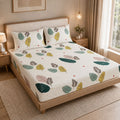 A bed dressed in a white fitted sheet and matching pillowcases featuring a colorful leaf print, styled in a warm, modern bedroom setting.