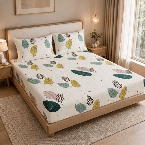 A bed dressed in a white fitted sheet and matching pillowcases featuring a colorful leaf print, styled in a warm, modern bedroom setting.